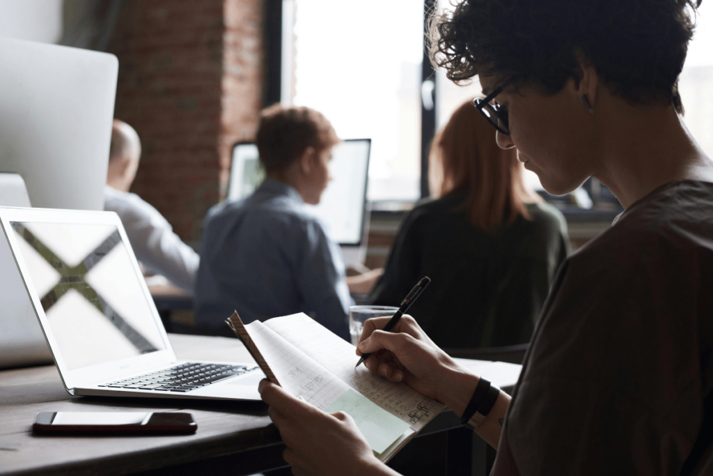 Curly-haired individual taking notes in a bustling office.