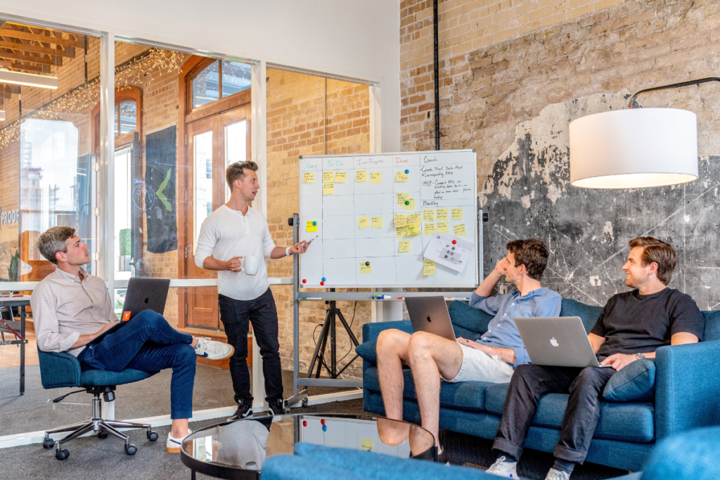 Team brainstorming session with four people discussing a whiteboard filled with sticky notes.