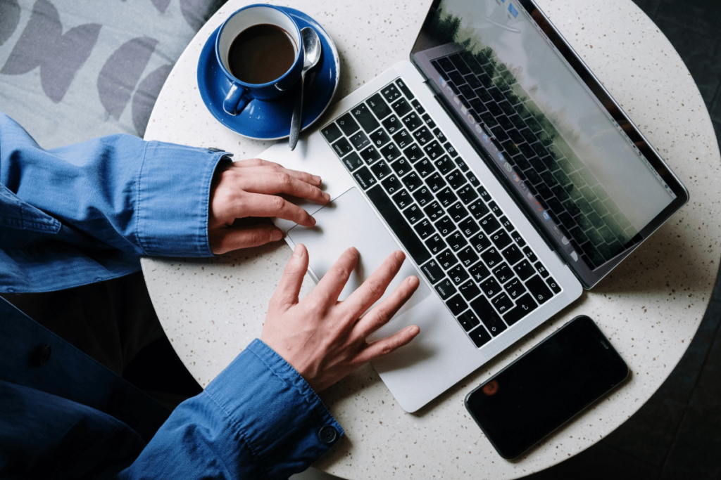 Top view of hands typing on a laptop with a blue cup of coffee and smartphone on the table.
