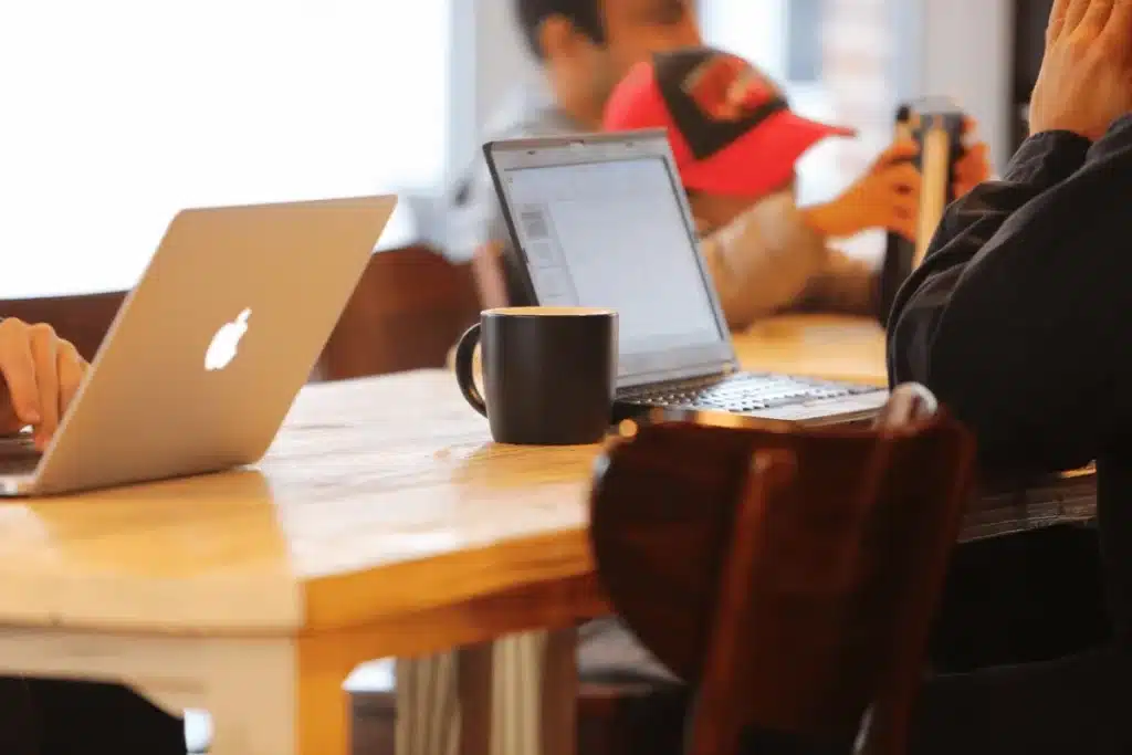 Person working on a laptop with a hot drink at a cafe with ambient lighting.