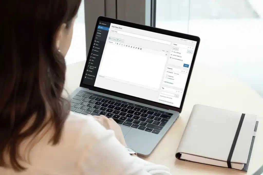 An individual using a laptop to manage a blog or website, with a notepad on the side for additional notes.