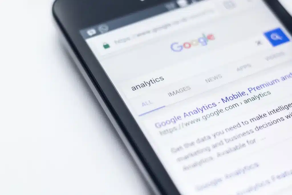Hand holding a phone with Google Analytics search result on a white background.