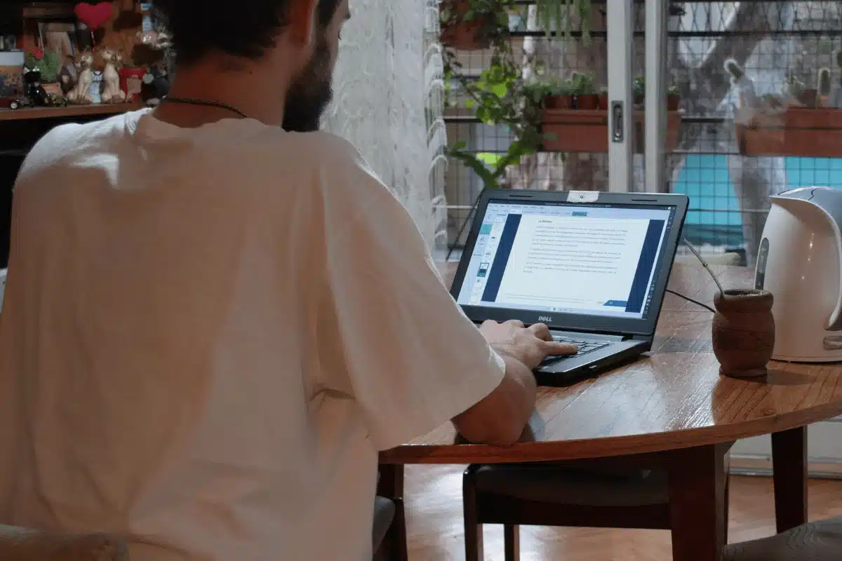 Person working on a laptop at a wooden table in a cozy home setting.