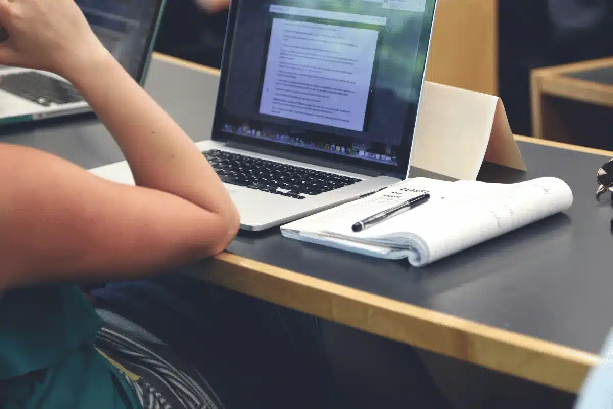Student studying with laptop and notebook on desk.