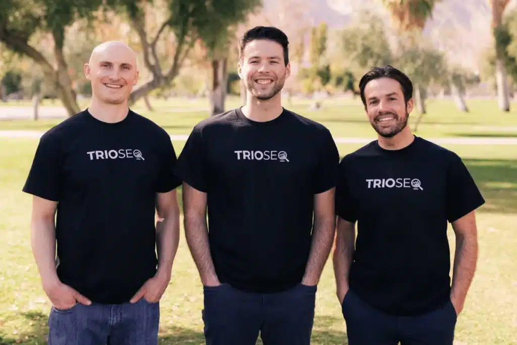Nathan, Steven and Connor wearing black T-shirts with "TRIOSEO" printed on them, standing in a sunny park with trees in the background.