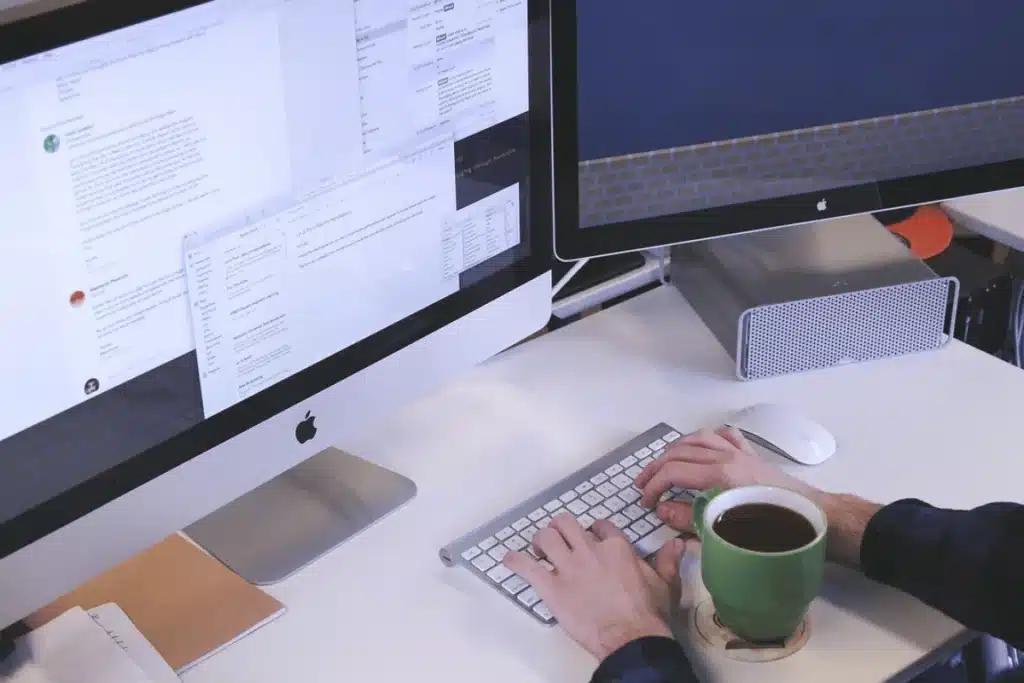 Professional multitasking with dual Apple monitors and a cup of coffee at work.