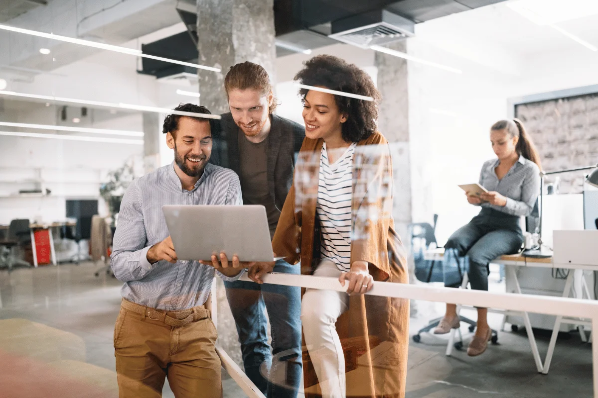 Three colleagues collaborating over a laptop in a modern office space.