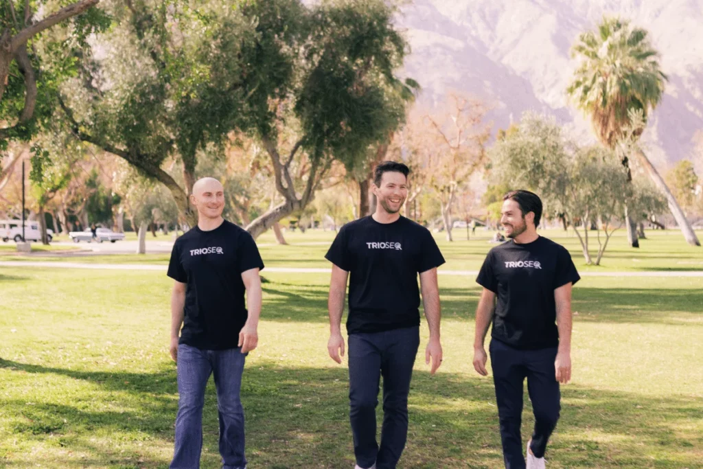Smiling trio Nathan, Steven, and Connor model black TRIOS&reg; t-shirts outside.
