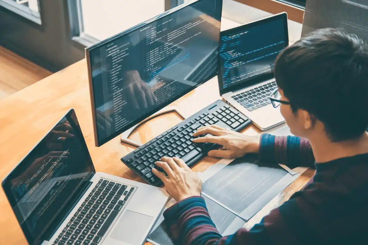 Software developer typing code on a keyboard surrounded by screens.