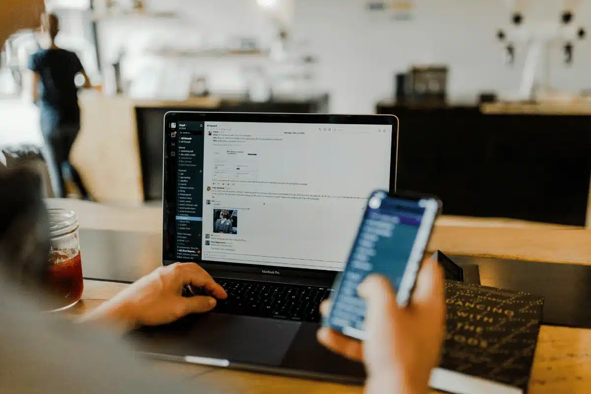 Close-up of hands working on a laptop and phone, managing online communications.