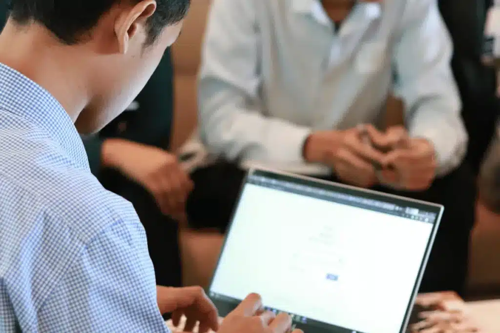 Person typing on a laptop during a group meeting.