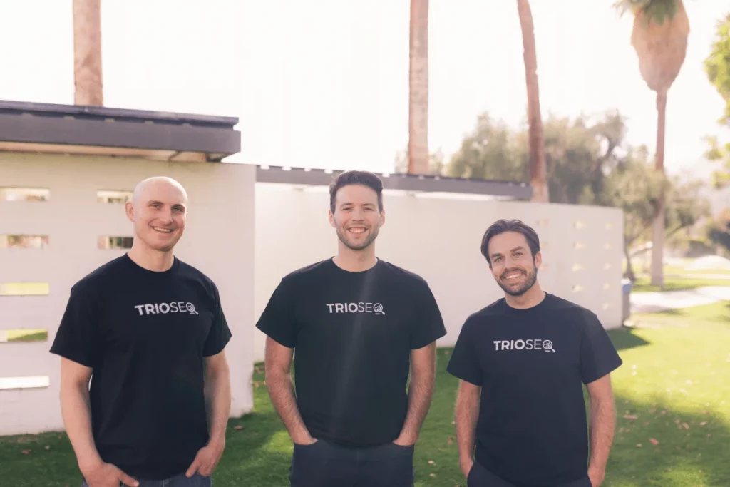 Smiling associates, Nathan, Steven, and Connor in TRIOS® tees, with sunny palms in the background.